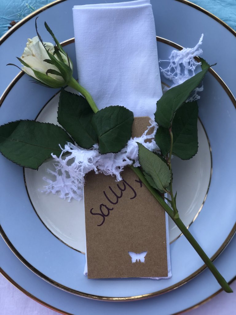 blue plate, single white rose, napkin and name place setting