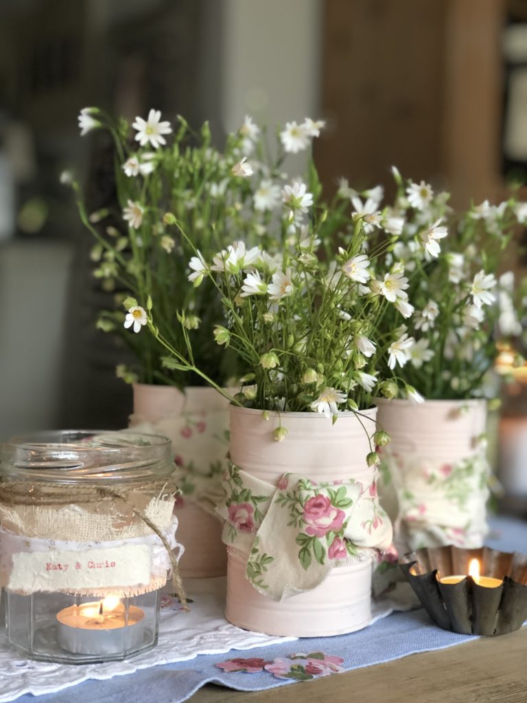 selection of pink tin cans with ribbon and glass jars hold summer flowers and candles for outdoor entertaining