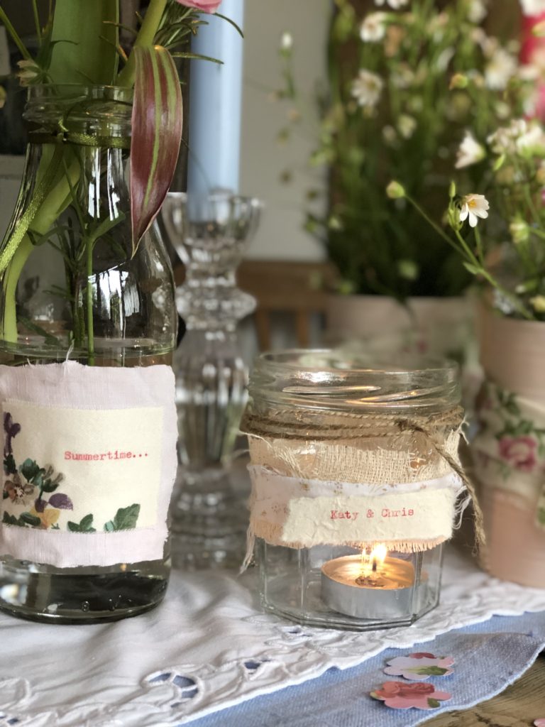 selection of pink tin cans with ribbon and glass jars hold summer flowers for outdoor entertaining