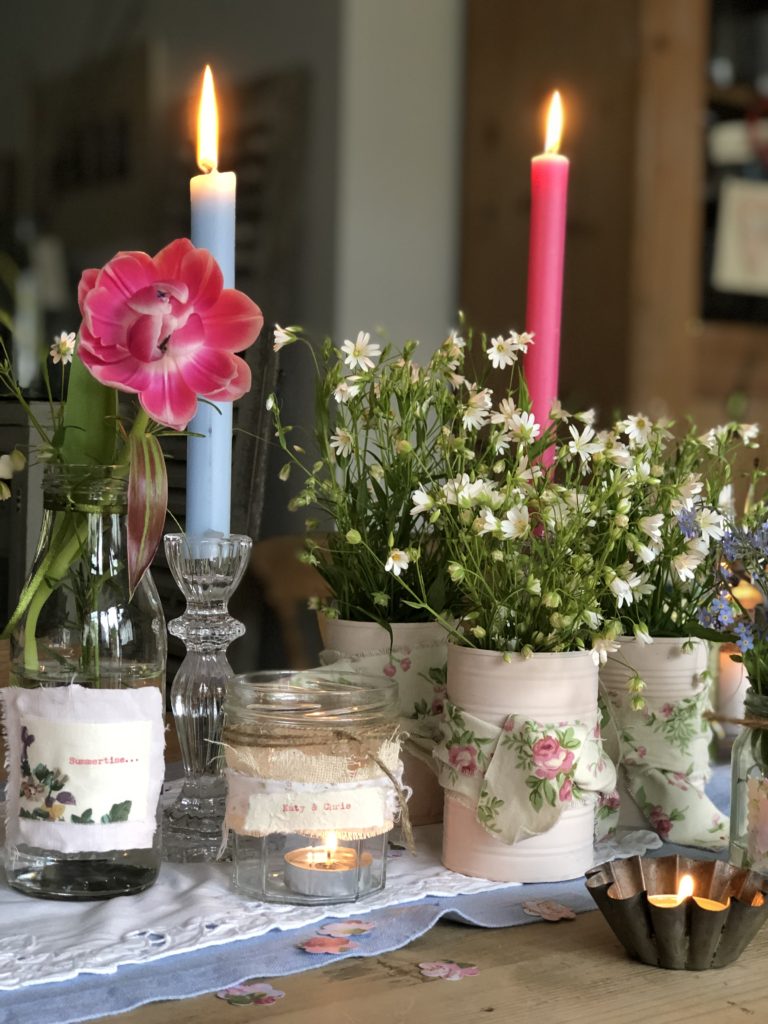 selection of pink tin cans with ribbon and glass jars hold summer flowers and candles for outdoor entertaining