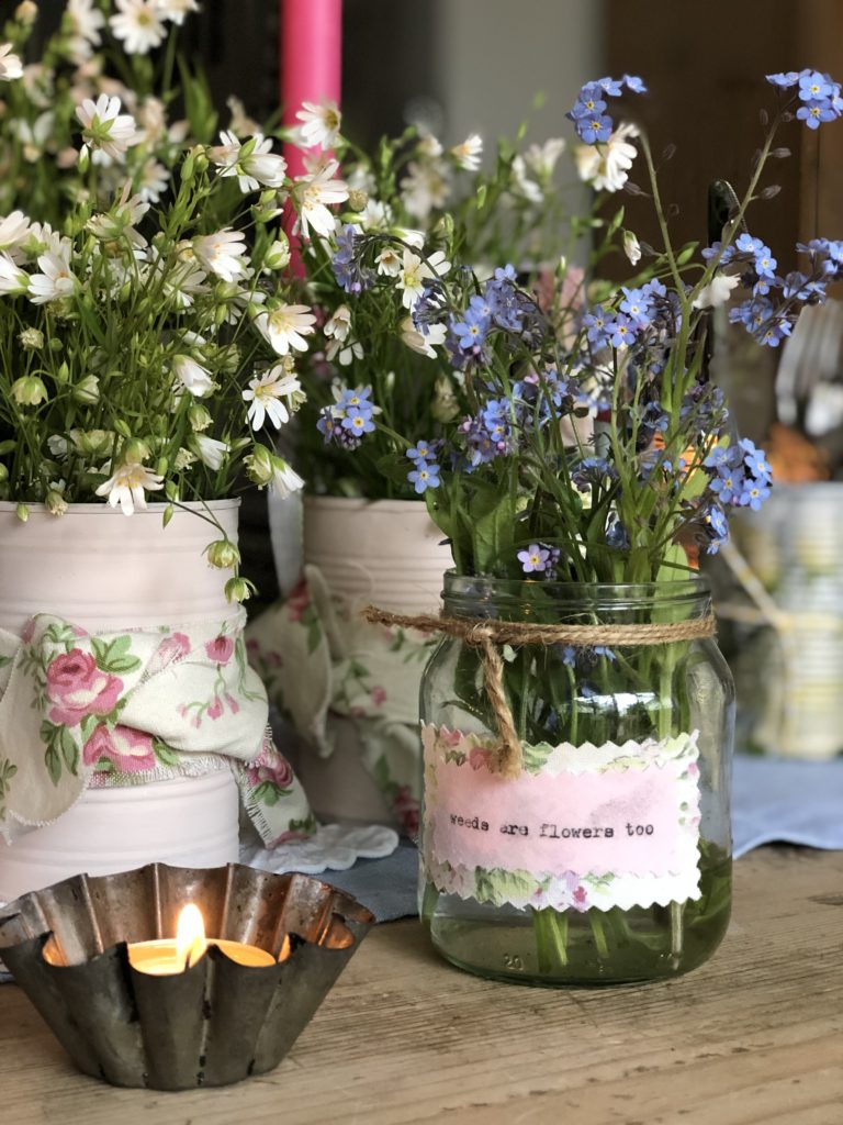 selection of pink tin cans with ribbon and glass jars hold summer flowers for outdoor entertaining