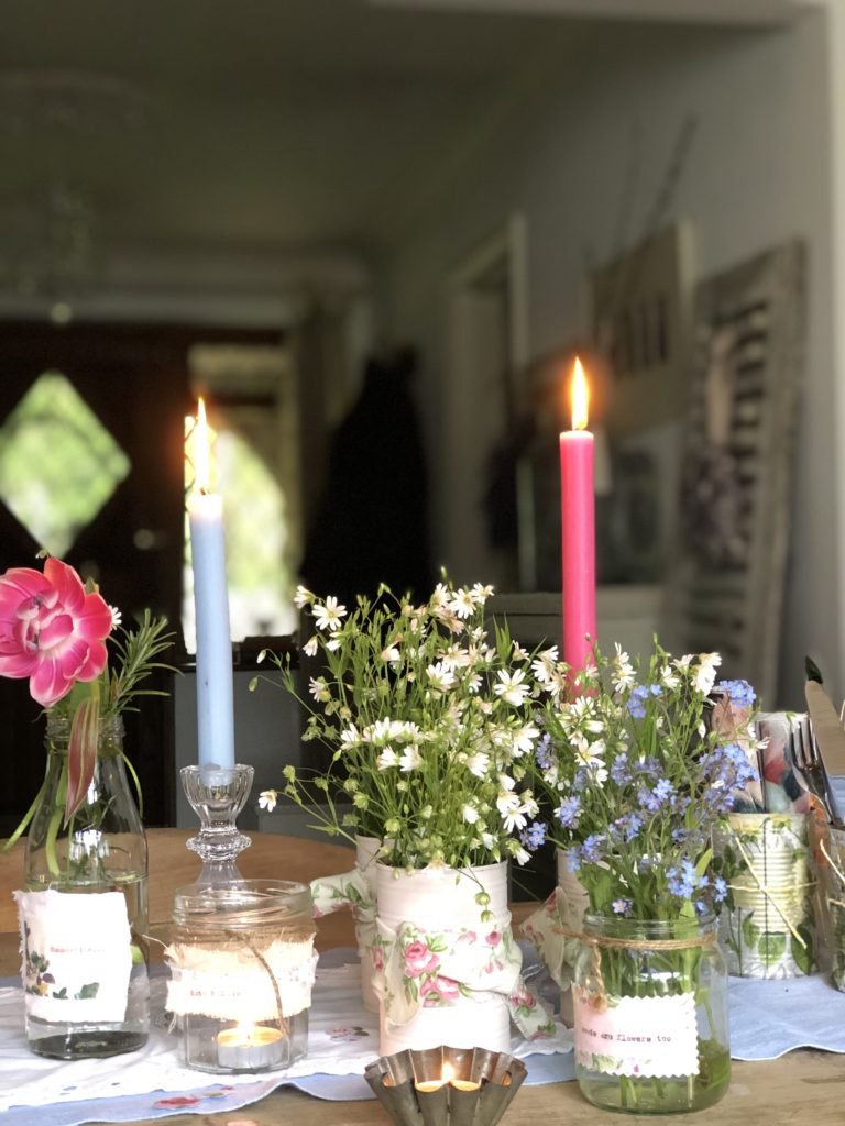 glass jars and bottles and tin cans hold summer flowers with pink and blue dinner candles