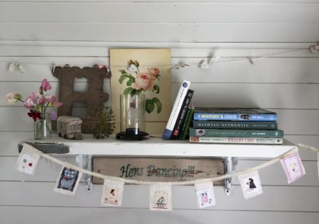 Painted shelf on painted tongue and groove wall dressed with pretty books, paintings and decoration and mini fabric bunting