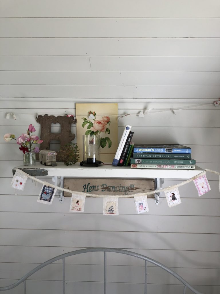 Painted shelf on painted tongue and groove wall dressed with pretty books, paintings and decoration and mini fabric bunting