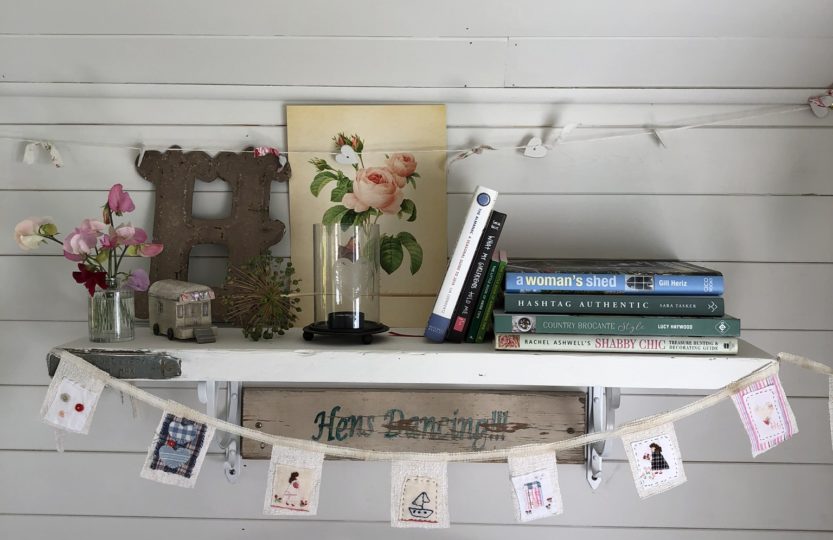 Painted shelf on painted tongue and groove wall dressed with pretty books, paintings and decoration and mini fabric bunting