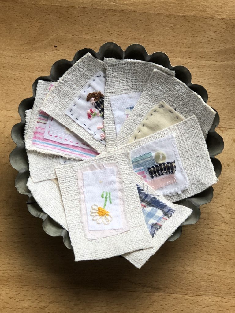 vintage flan tin containing pieces of embroidered fabric in a pinwheel