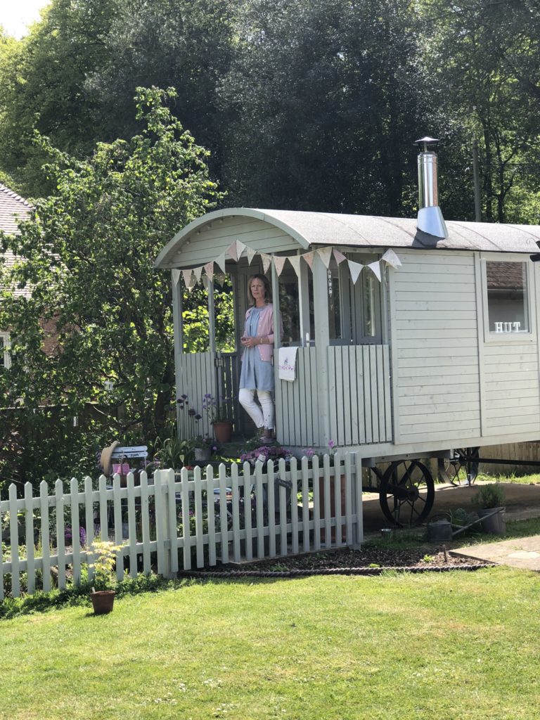 Lady on steps of pretty painted shepherds hut with picket fence 