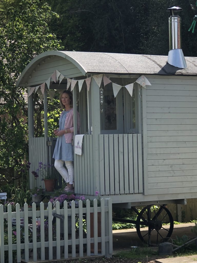 Lady on steps of pretty painted shepherds hut with picket fence