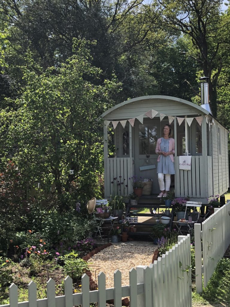 Lady on steps of pretty painted shepherds hut with picket fence