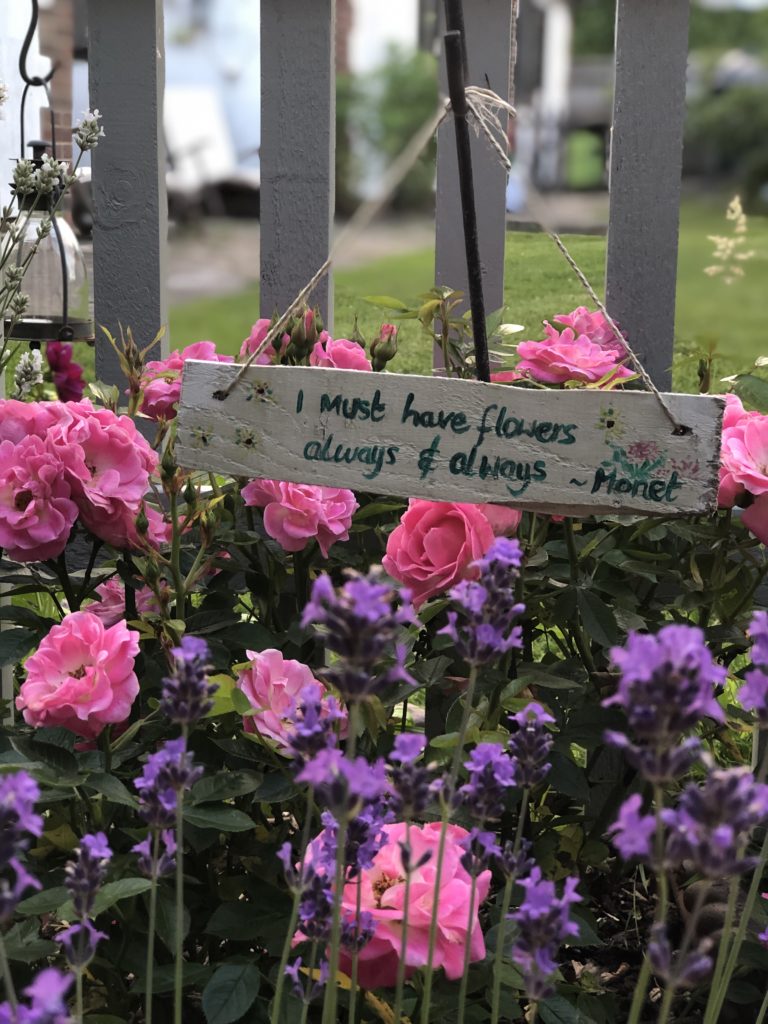 Monet garden quote painted on wooden garden sign amongst roses and lavender