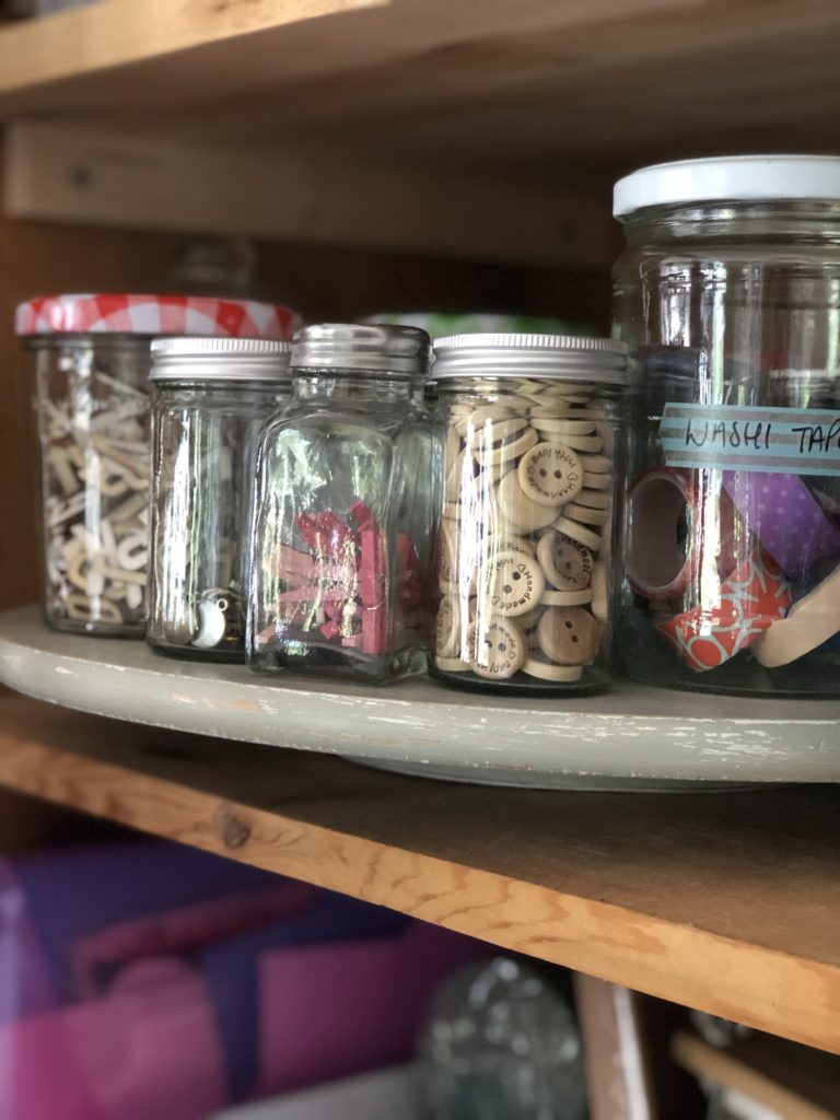 variety of glass storage jars on lazy susan in craft cupboard