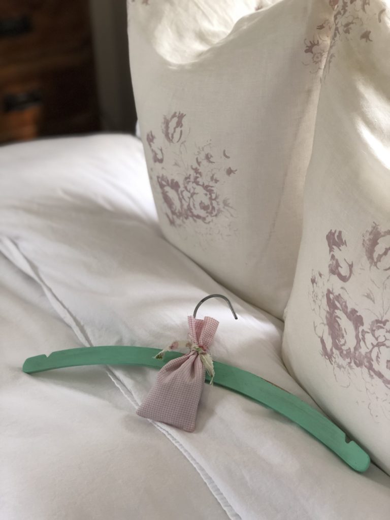 lavender bag and green painted wooden coat hanger on white bedding with cabbages and roses Hately cushions