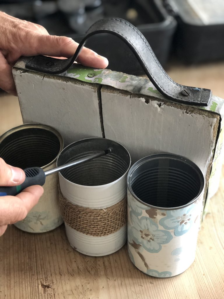 decorated tin cans being drilled to white scaffold board