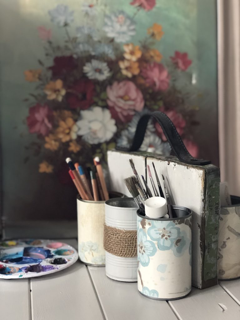 tin can organiser with artists brushes and equipment and pretty oil flower painting