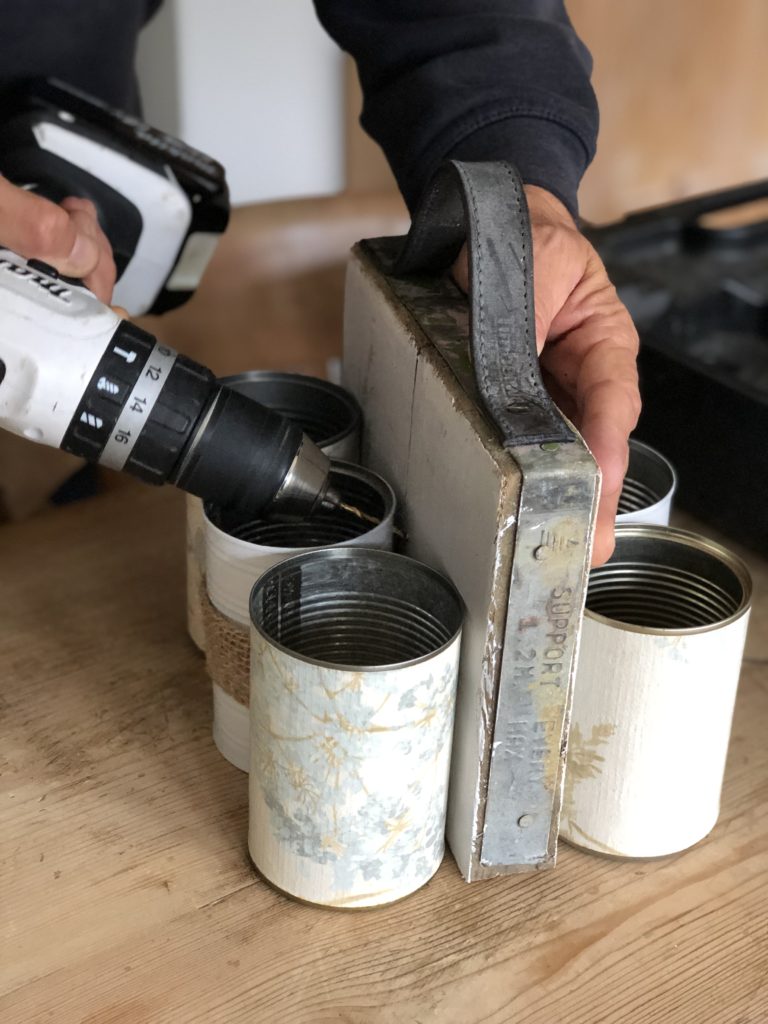 decorated tin cans being drilled to white scaffold board 