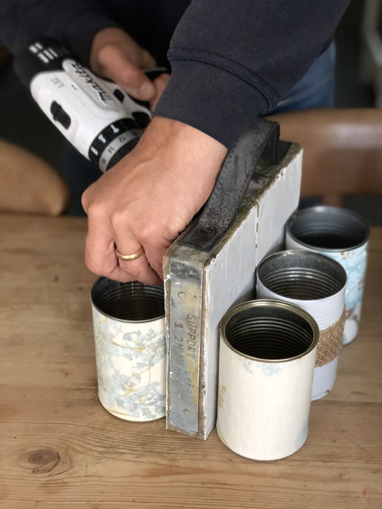 decorated tin cans being drilled to white scaffold booard