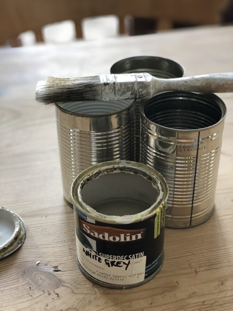 four empty tin cans and paint and brush