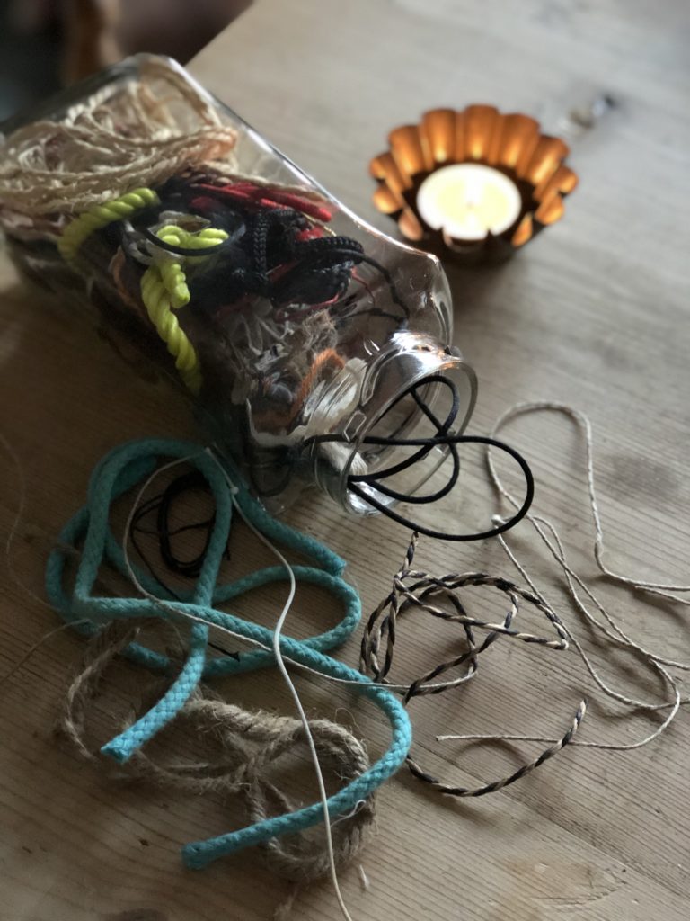 variety of off cuts of string spilling from glass jar with tealight