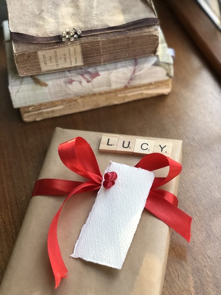 red bow on brown paper wrapped gift with letter tiles and tag