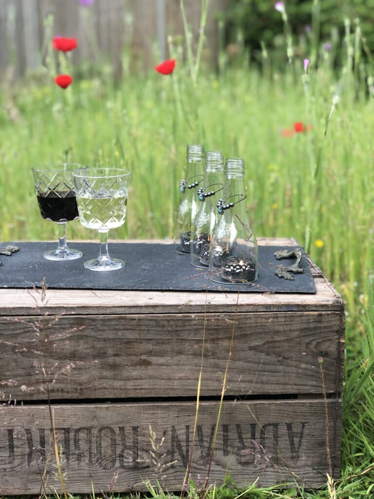 glasses of wine on glass bottle decoration on wooden crate in wildflower meadow