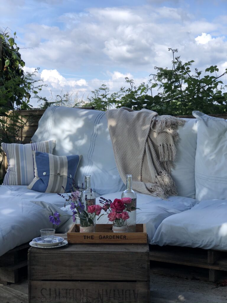 pallet sofa with cushions and throw and recycled wine project in pretty garden setting