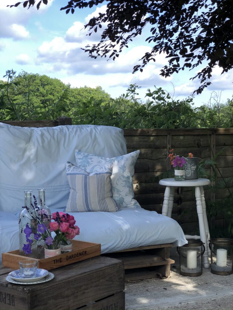 pallet sofa with cushions and throw and recycled wine project in pretty garden setting