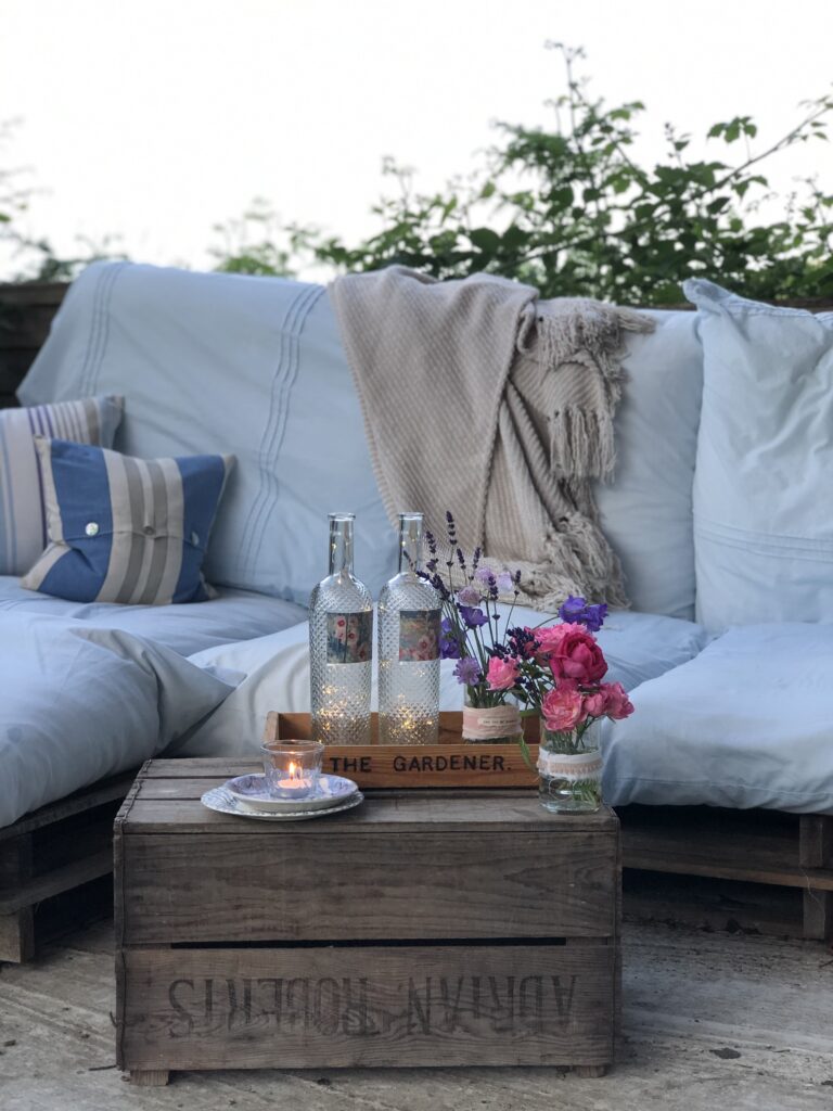 pallet sofa with cushions and throw and recycled wine project in pretty garden setting