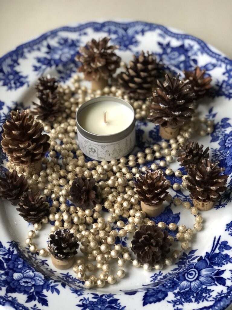 beads and pine cones on blue and white platter with candle