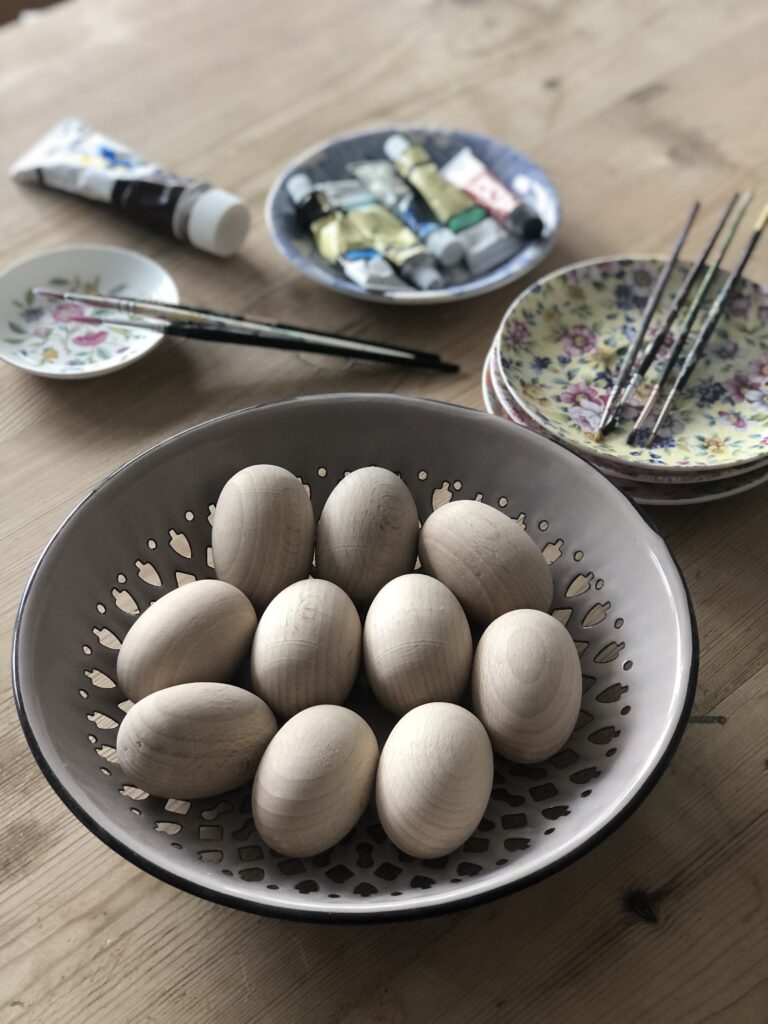 wooden craft eggs in bowl with painting equipment to create homemade easter table decoration