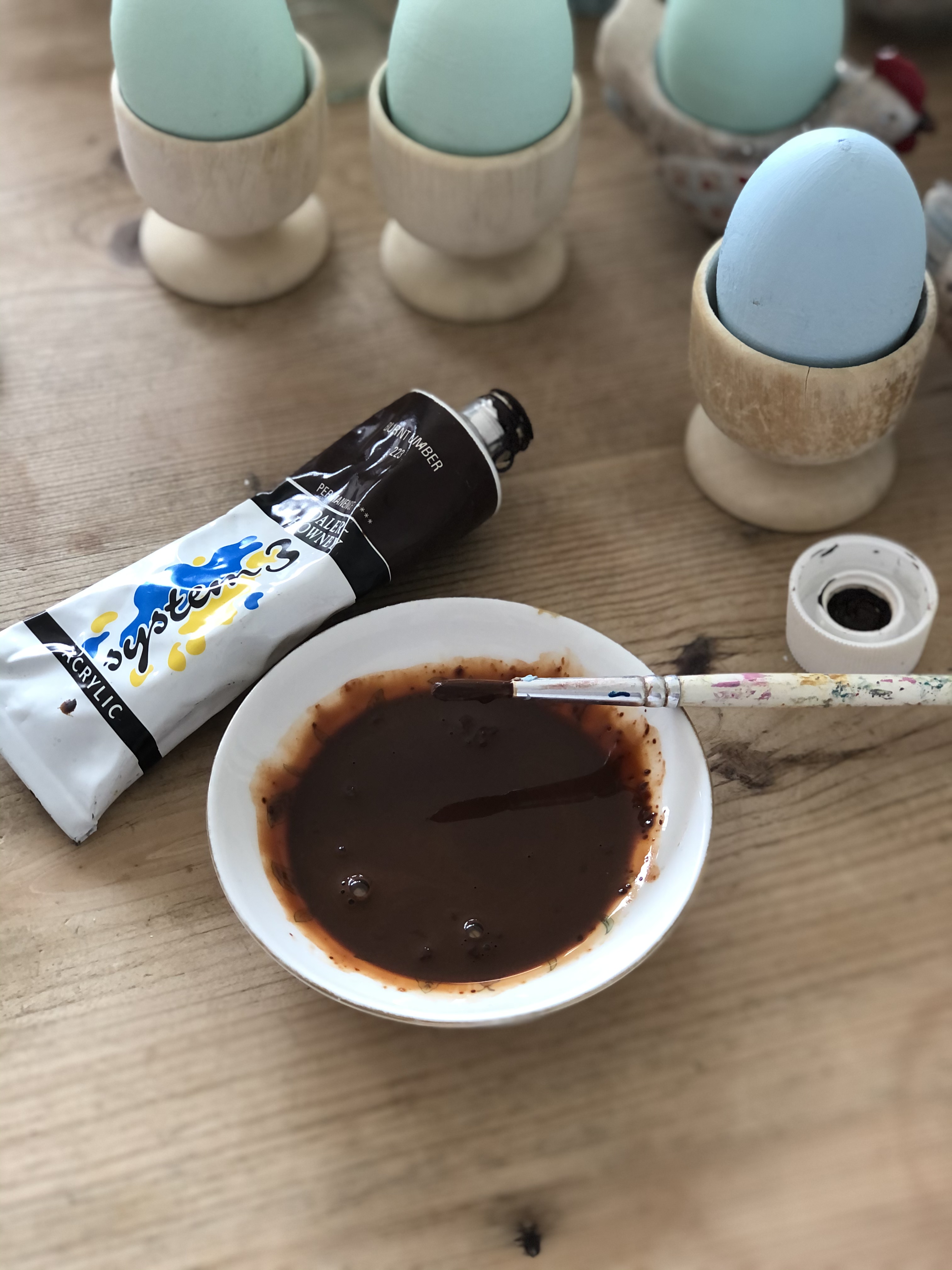 mixing brown paint in teaplate with wooden painted eggs in background