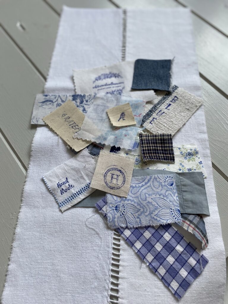 arranging blue and white fabric scraps on white linen for sampler