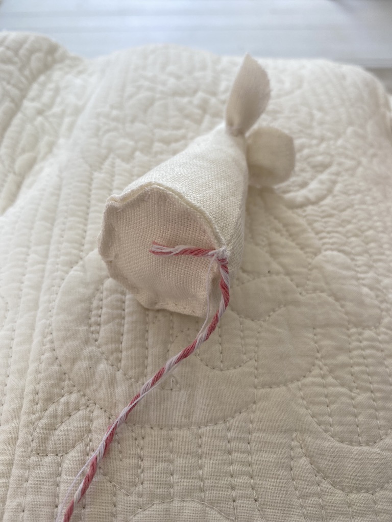 adding a pink string tail to the base of a white linen fabric mouse