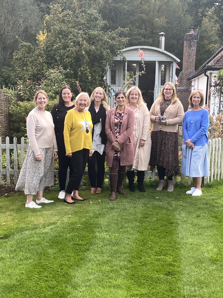 eight smiling ladies stand in front of pretty Shepherds Hut in cottage garden setting