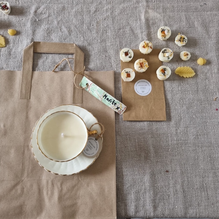 flatlay of tea cup candles, soy wax melts in variety of shapes on top of brown paper bags on linen clothed table