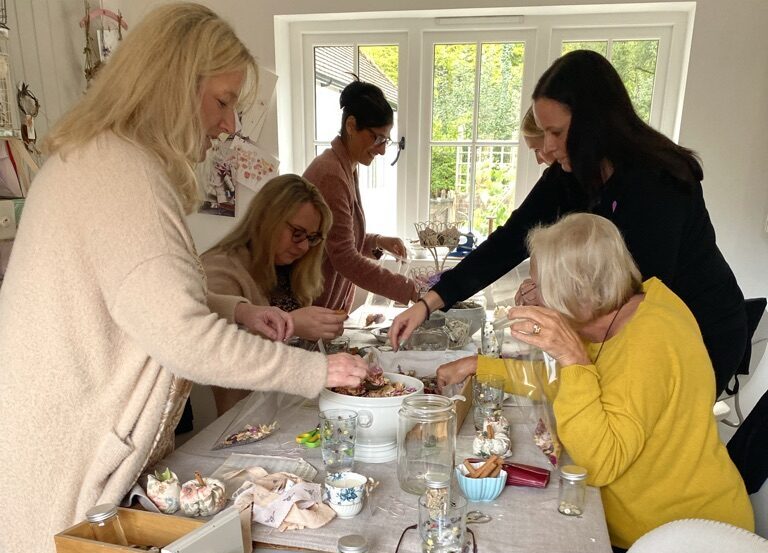 ladies making pot pourri from bowls of garden petals with cups, jars and fabric apples around them