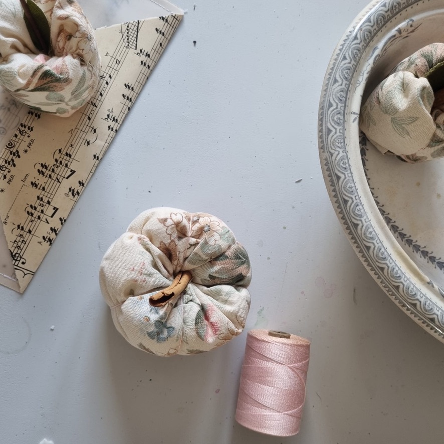 flat lay of fabric pumpkin, fabric apples, pink thread, music paper and part of vintage pot