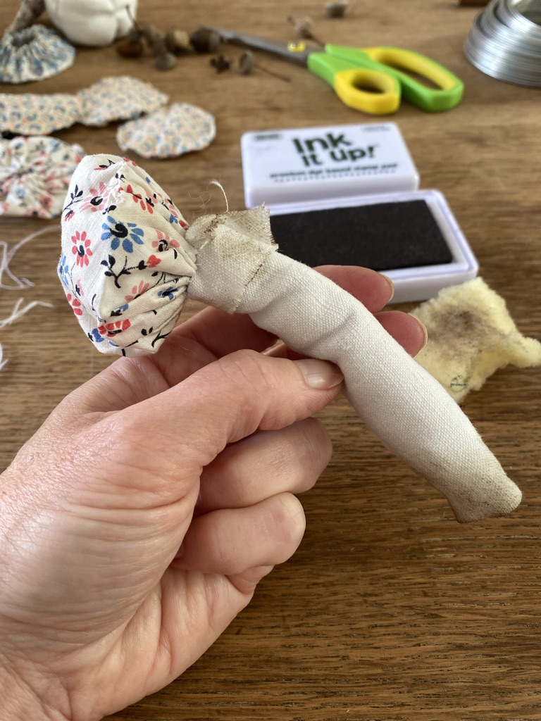 adding ink to a fabric mushroom to create an appearance of dirt on a wooden craft table full of craft ephemera