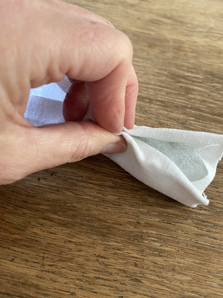 fingers hold together white fabric ready to sew a seam on a fabric mushroom stem