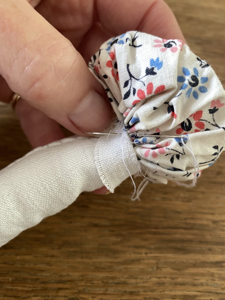 attaching the floral suffolk puff cap of a textile toadstool to the white linen stem and sewing in place