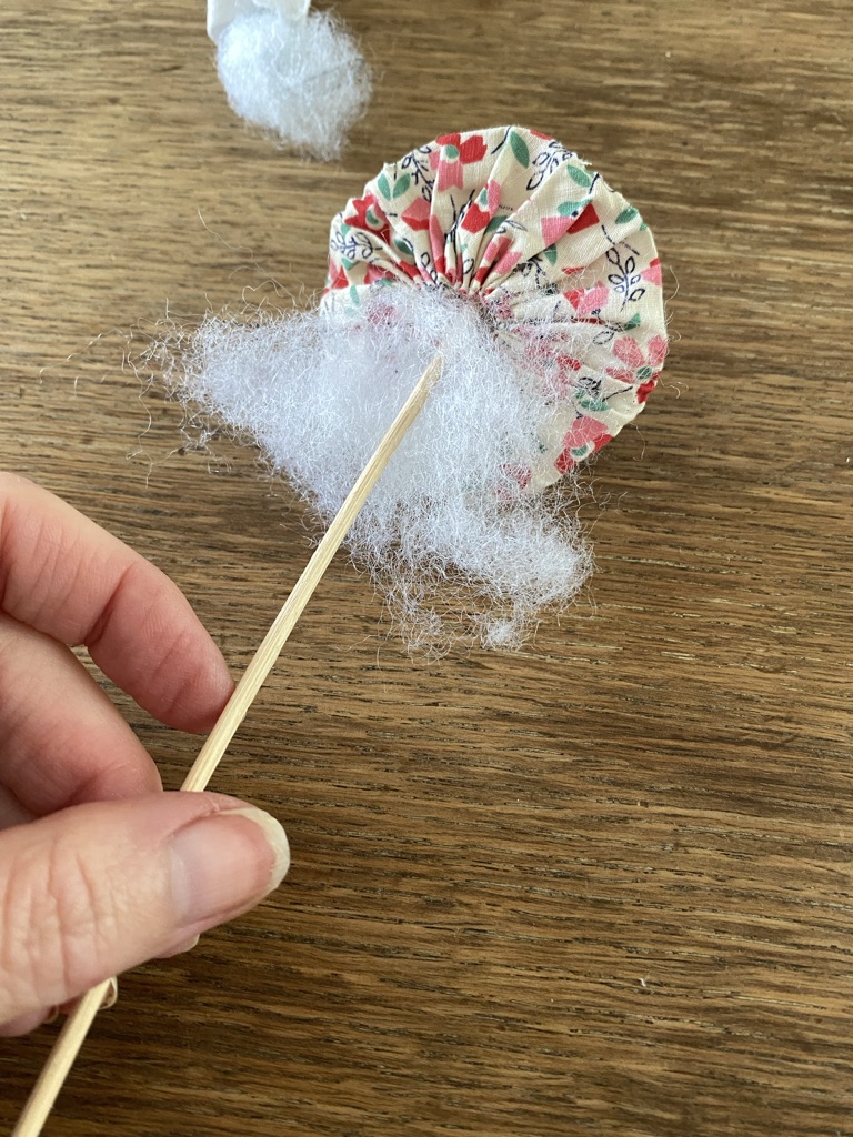 poking toy stuffing into a suffolk puff with a wooden skewer