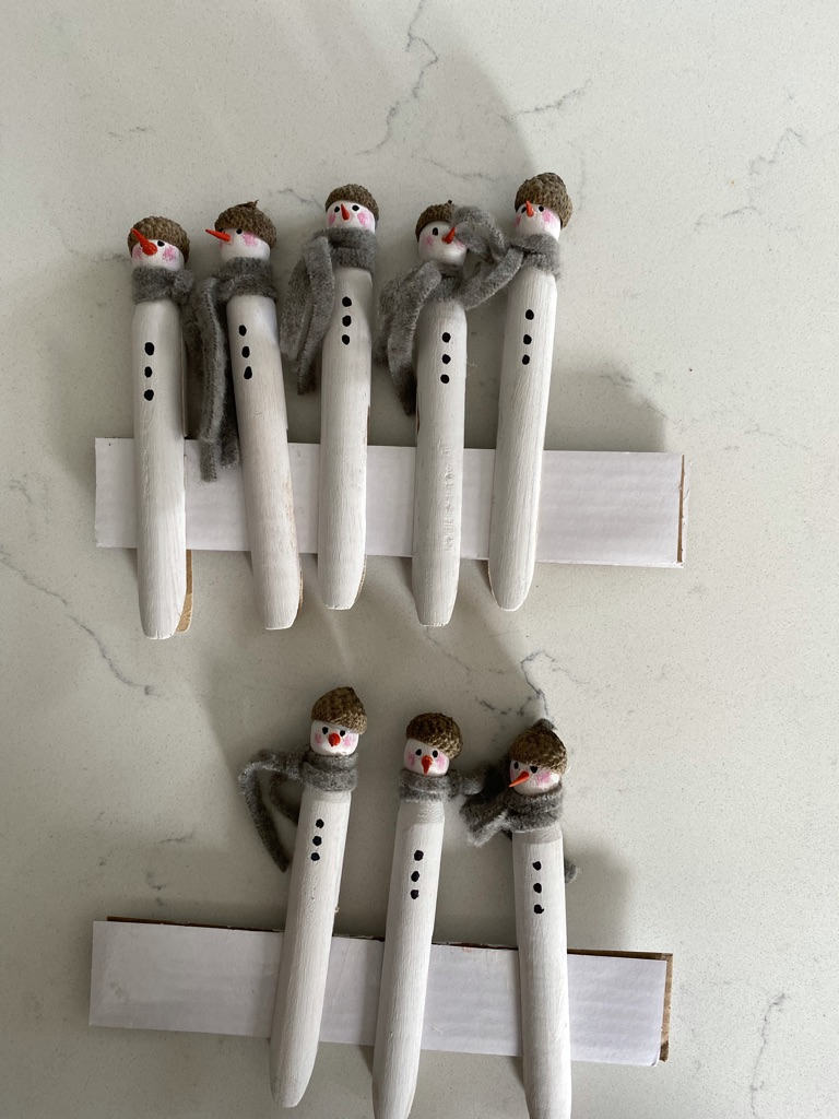 eight homemade painted peg snowmen fixed to white card