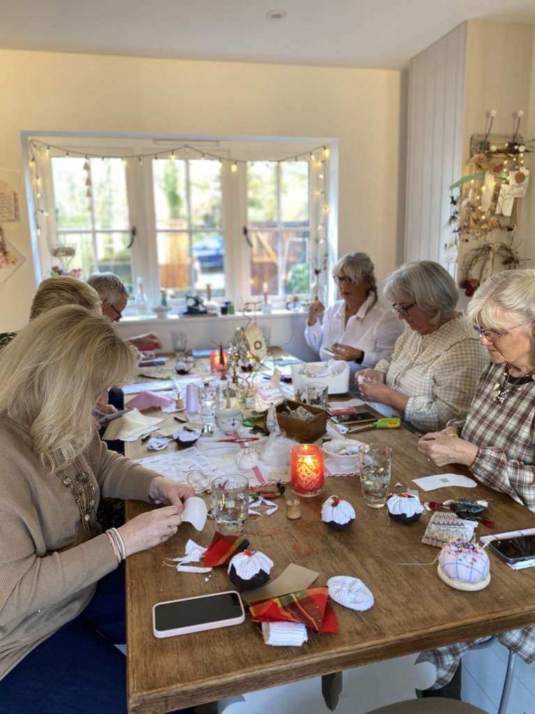 ladies crafting at table covered with fabrics, candles, crafty Christmas trees and other crafting ephemera