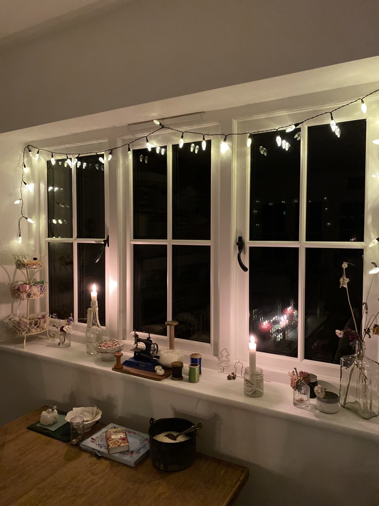 fairy lights and candles adorn a window of a homespun craft room