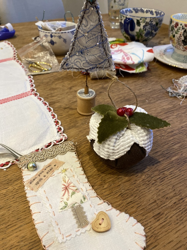 craft table with mugs, bowls, fabric Christmas trees, stockings and puddings