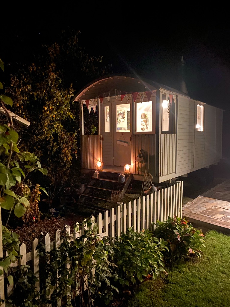 beautiful shepherds hut decorated with bunting in cottage garden at night lit up by candles and lights