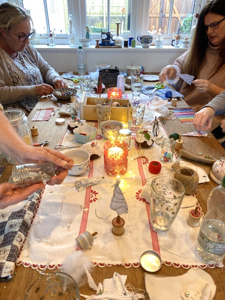 ladies crafting at table covered with fabrics, candles, crafty Christmas trees and other crafting ephemera