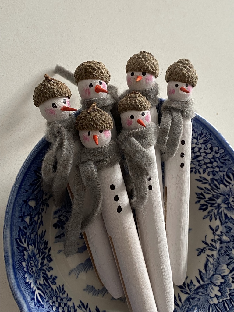 sixhomemade painted peg snowmen sit in blue and white bowl