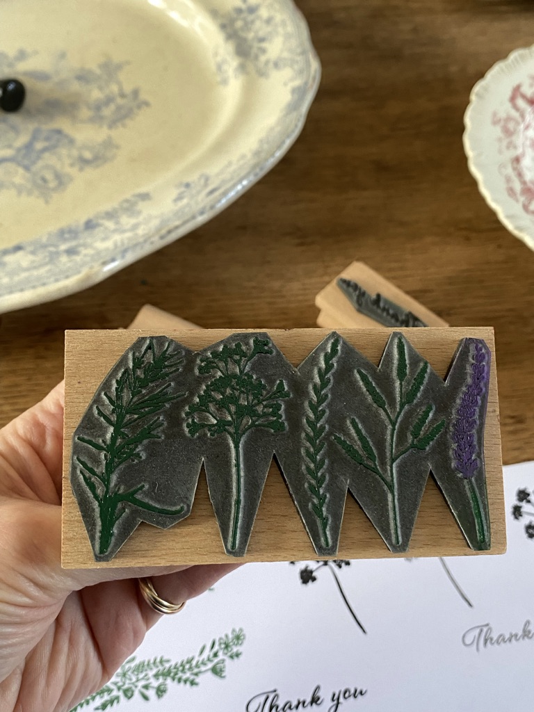 hand shows rubber design of floral craft stamp with vintage bowls and stamped paper in background