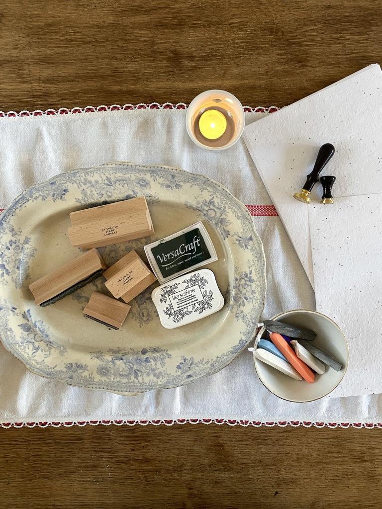 rubber stamps, ink pads, candle, wax seals and wax and paper on red and white runner on craft table