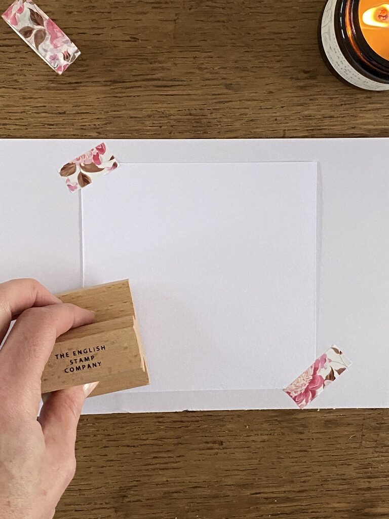 hand stamps a craft rubber stamp onto paper secured with washi tape with candle in background